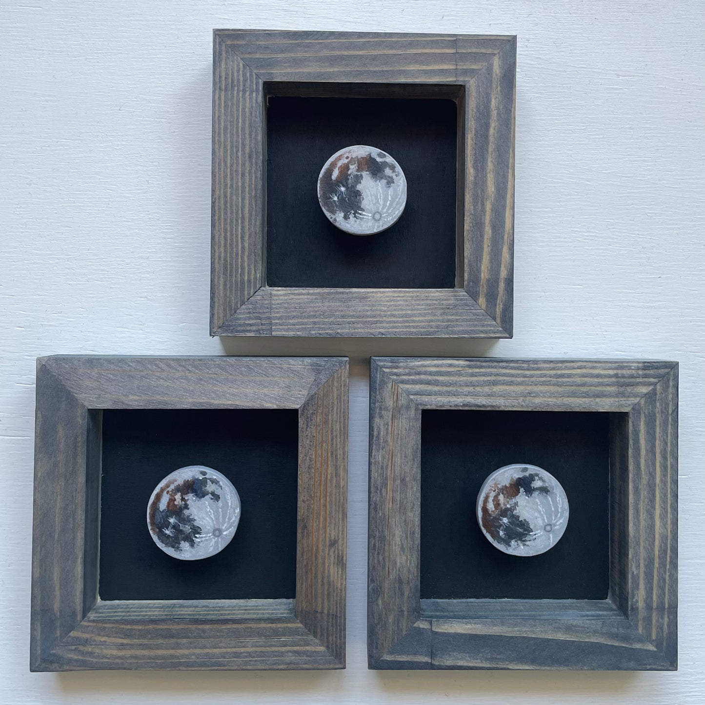 All three grey stained frames with black background. Floating in each shadowbox is a hand-painted clay Moon