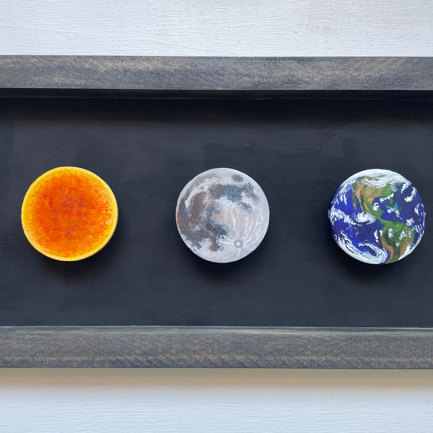 A closer view of the Sun, Moon, and Earth clay disks mounted in the frame.