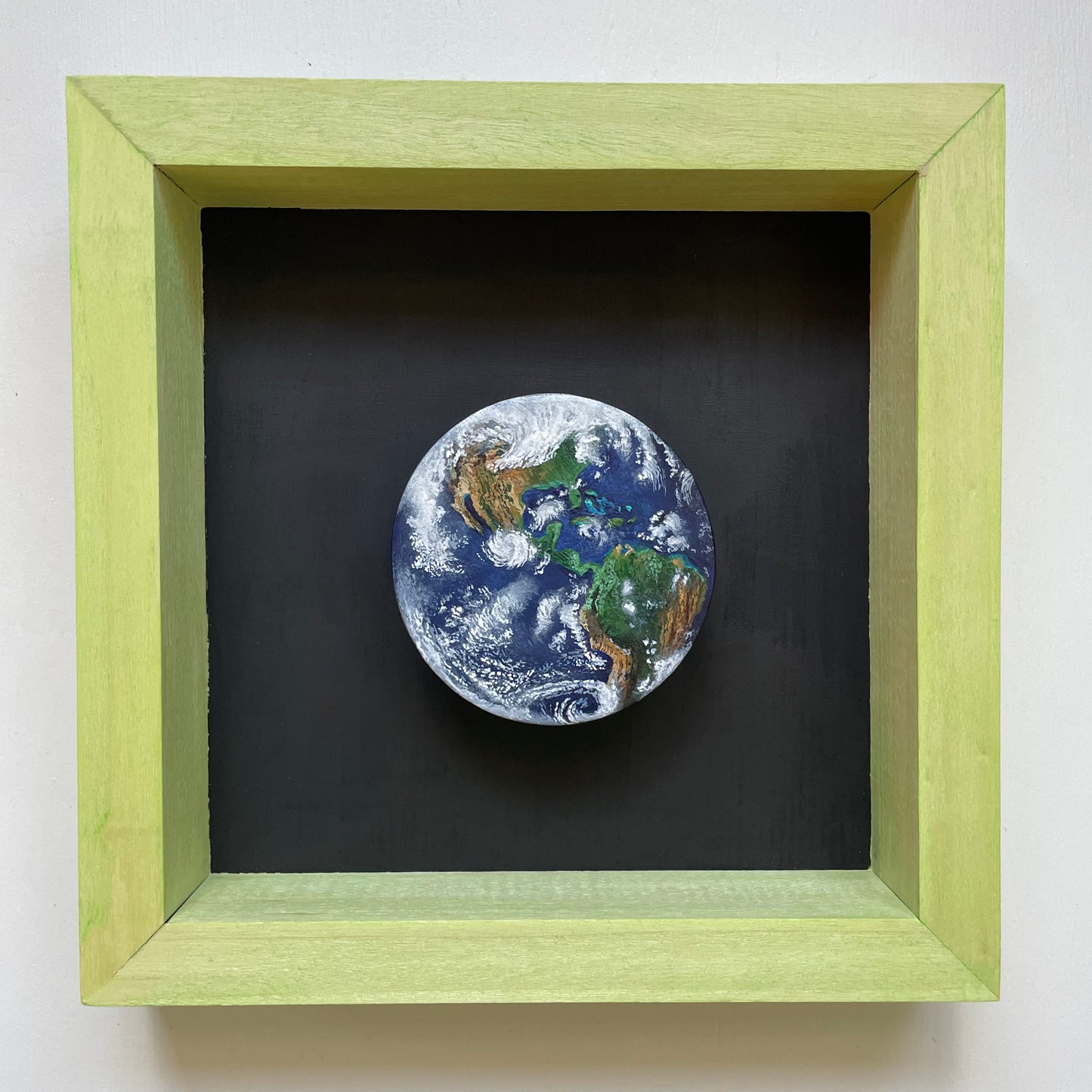 Clay disk painted like Earth with North and South American in view. Mounted in a shadow box stained light green with a black background.