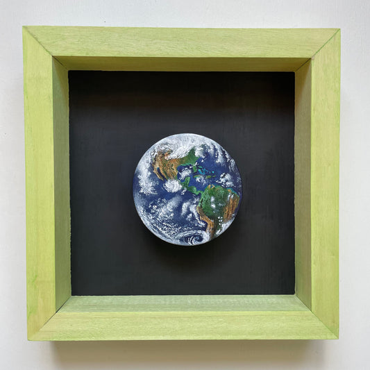 Clay disk painted like Earth with North and South American in view. Mounted in a shadow box stained light green with a black background.