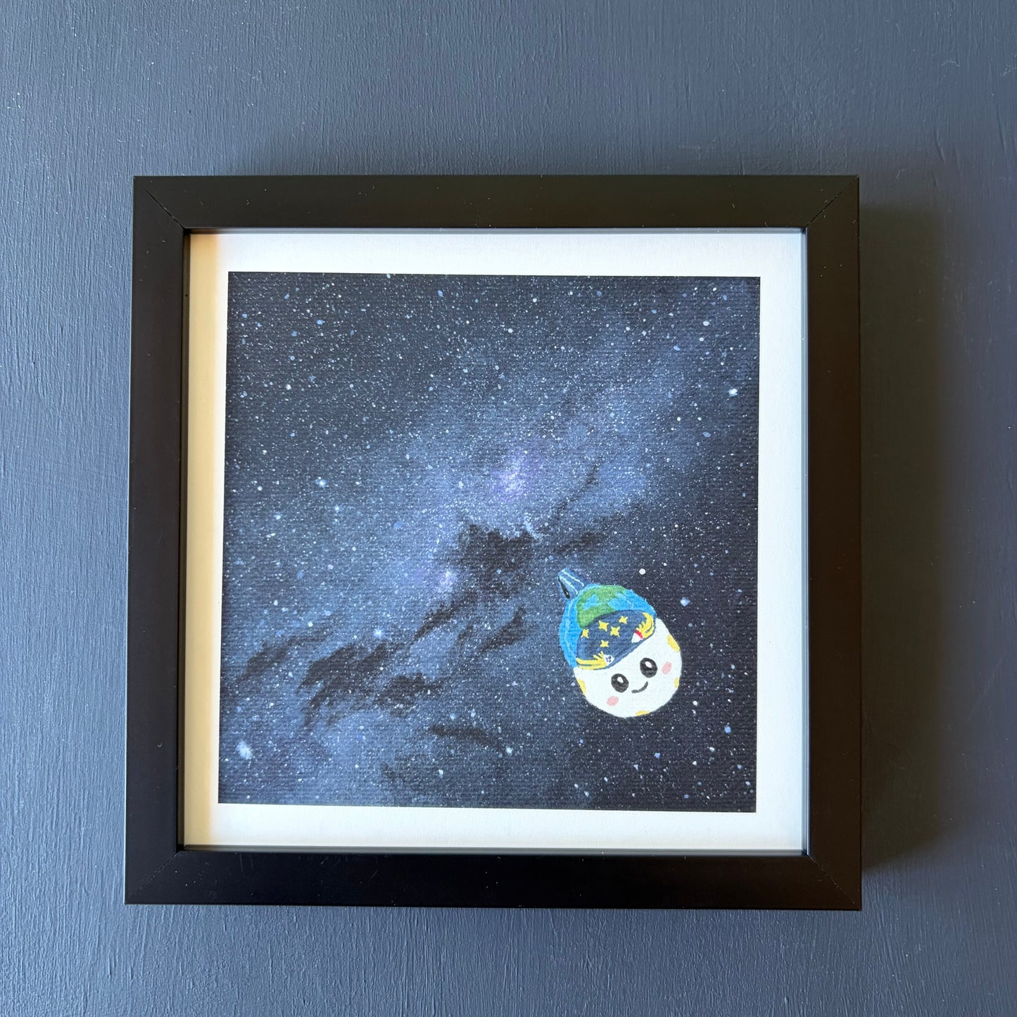Mini print in black frame of the Milky Way. A dense blue and purple star field. Rise is painted in the bottom right corner.