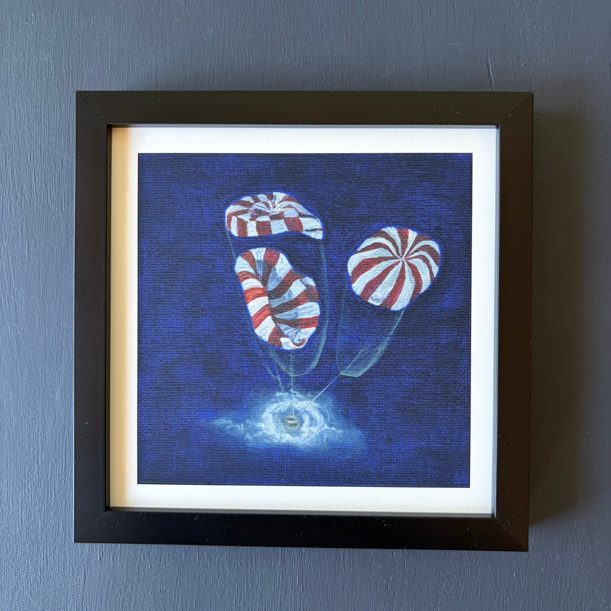 mini print in black frame of 3 red and white striped parachutes deploying on Orion capsule landing in ocean