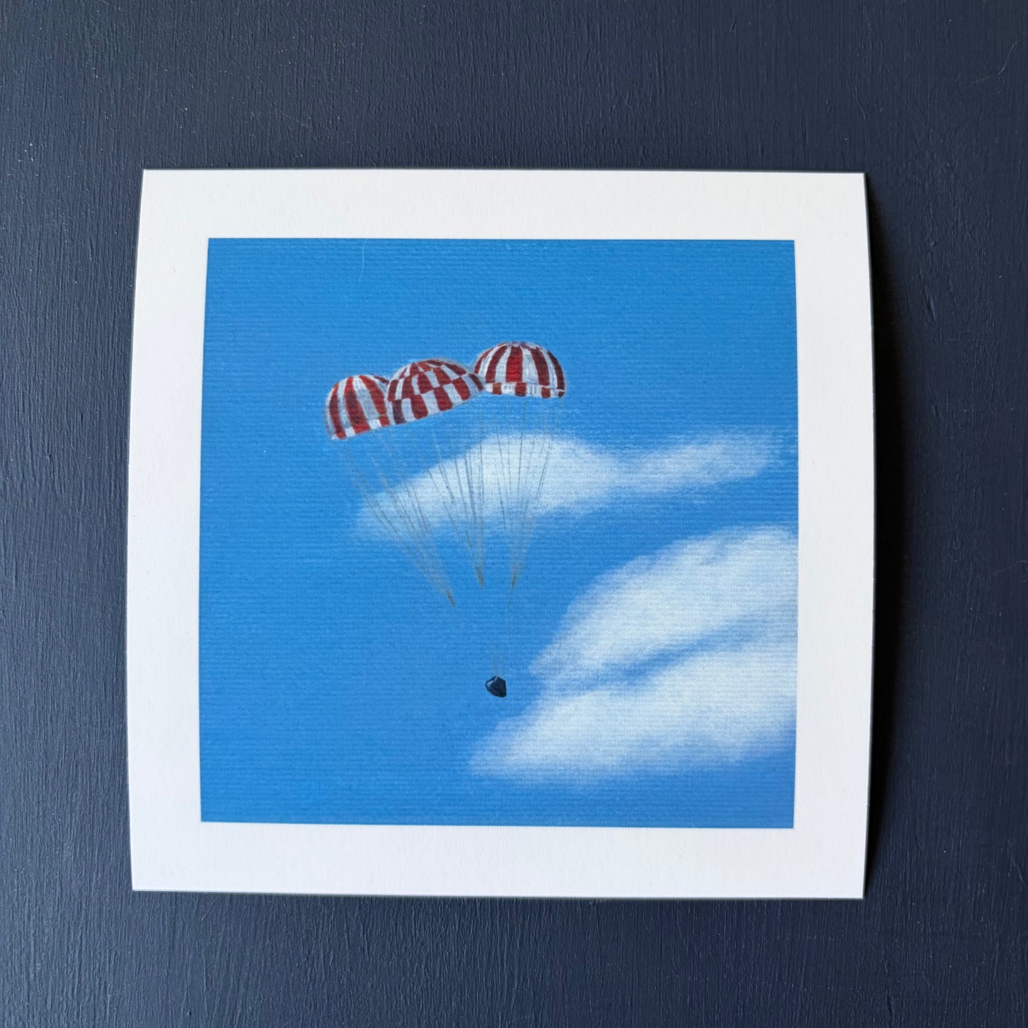 mini print of 3 red and white striped parachutes descending against a blue sky with clouds