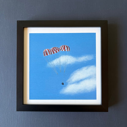 mini print in black frame of 3 red and white striped parachutes descending against a blue sky with clouds