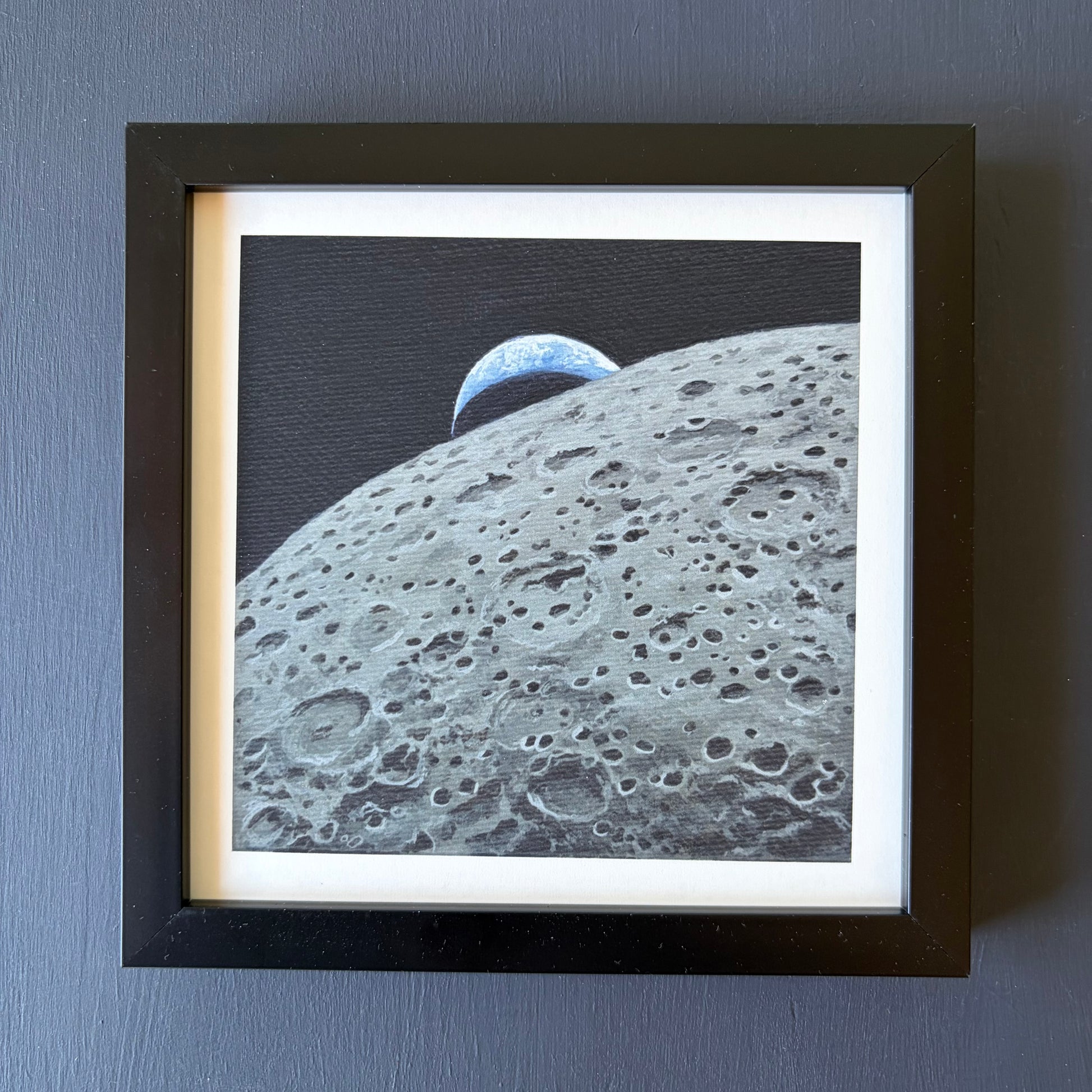 Mini print in black frame of the lunar surface in the foreground and a crescent Earth setting behind the Moon