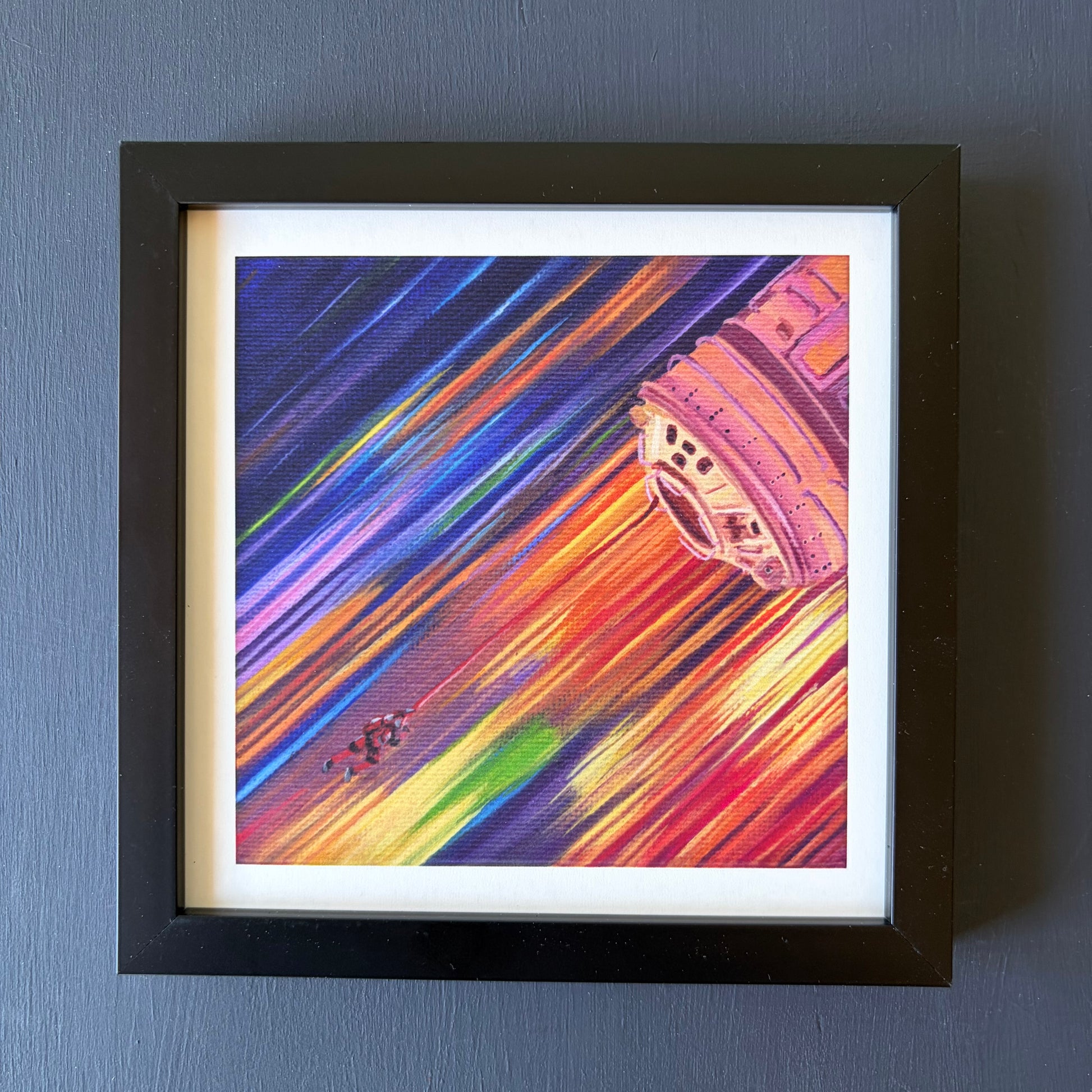 mini print in black frame of a tiny astronaut and spaceship with a background of colorful streaks