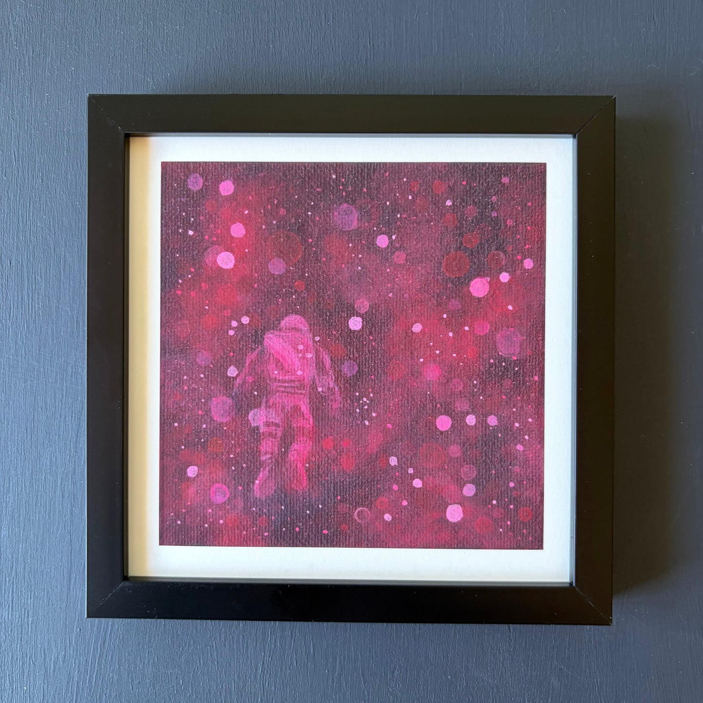 Mini print in black frame of astronaut floating surrounded by red and pink bokeh