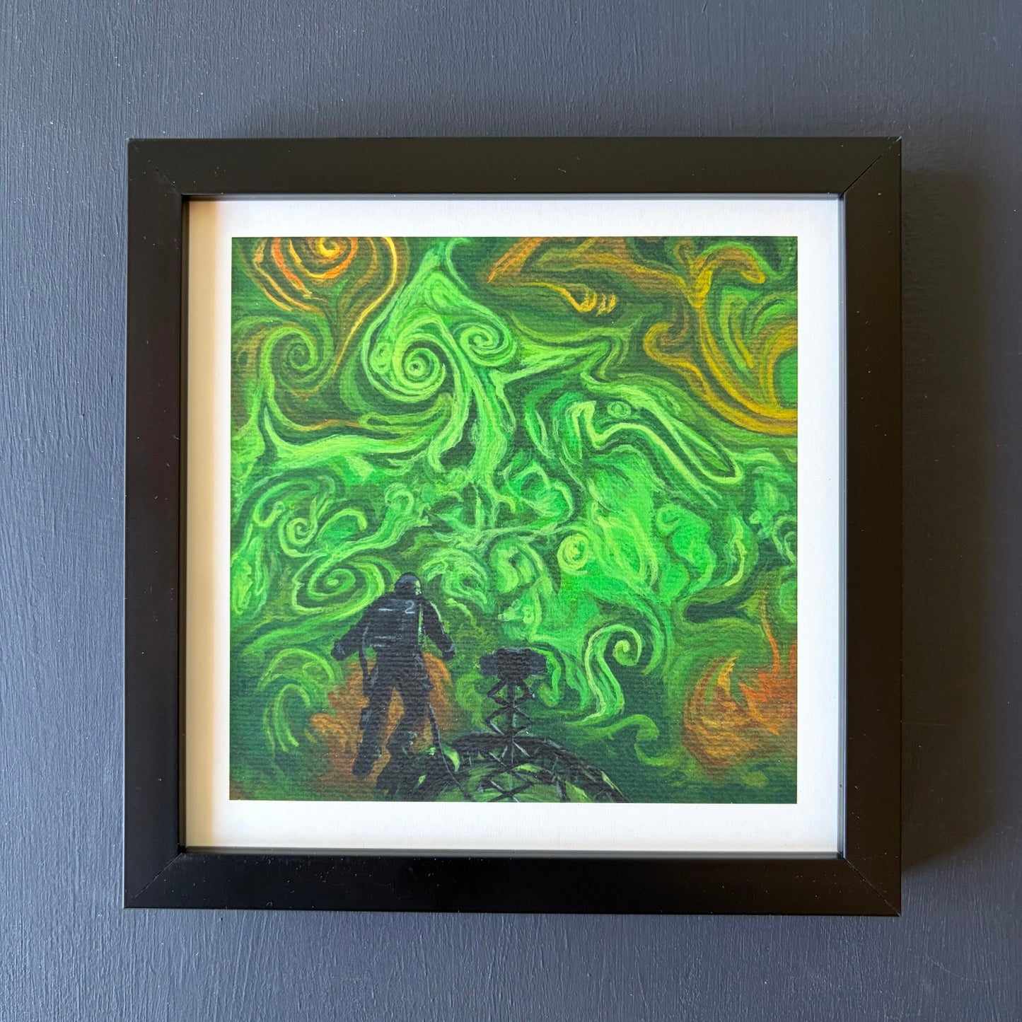 Print in black frame of swirling green and orange clouds. An astronaut floats above a spaceship at the bottom of the piece.