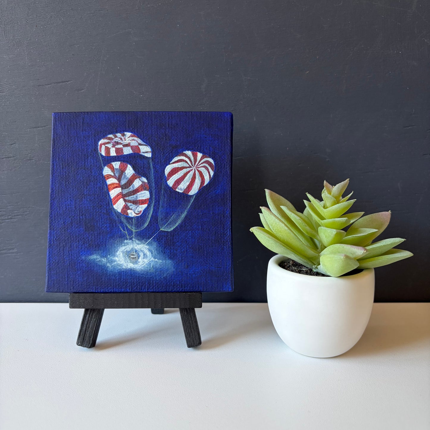 mini painting on easel of 3 red and white striped parachutes deploying on Orion capsule landing in ocean