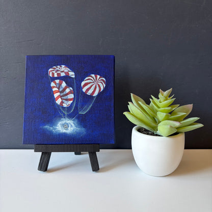 mini painting on easel of 3 red and white striped parachutes deploying on Orion capsule landing in ocean