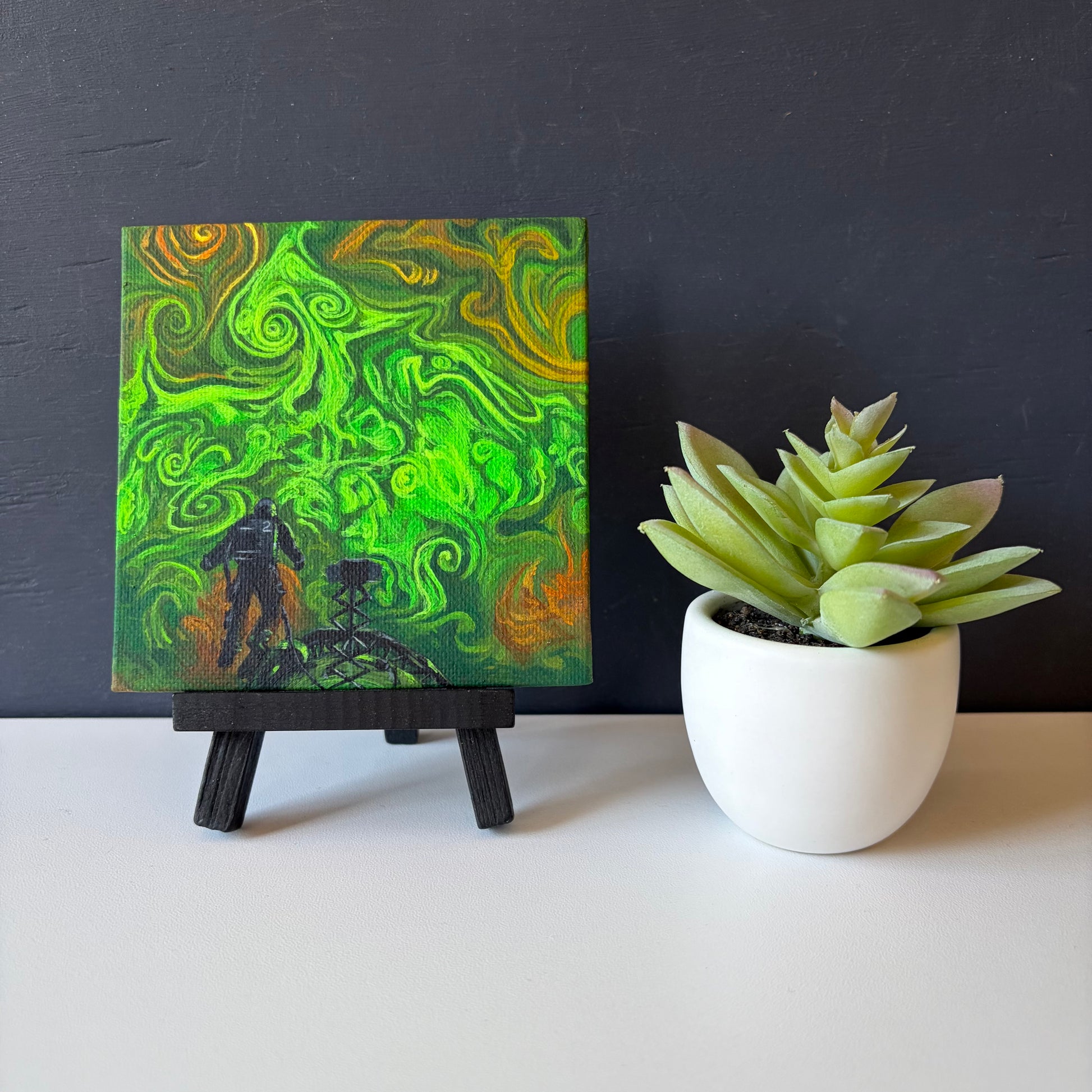 mini painting on easel with swirling green and orange clouds. An astronaut floats above a spaceship at the bottom of the piece.