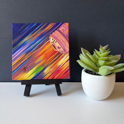 mini painting on easel of a tiny astronaut and spaceship with a background of colorful streaks