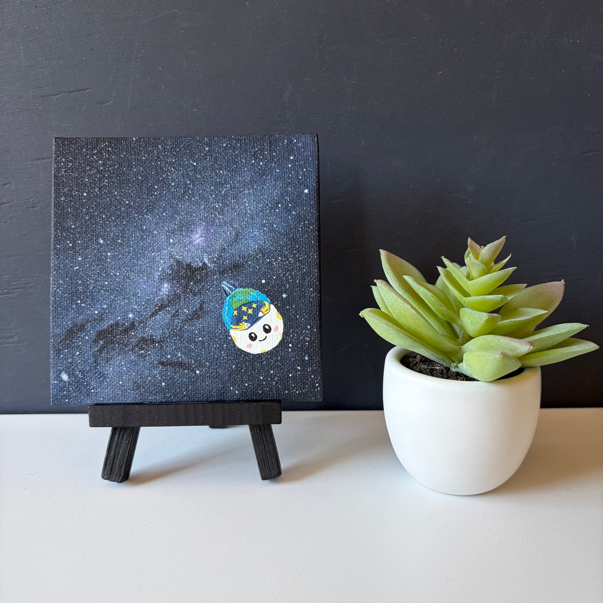 mini painting on easel of the Milky Way. A dense blue and purple star field. Rise is painted in the bottom right corner.
