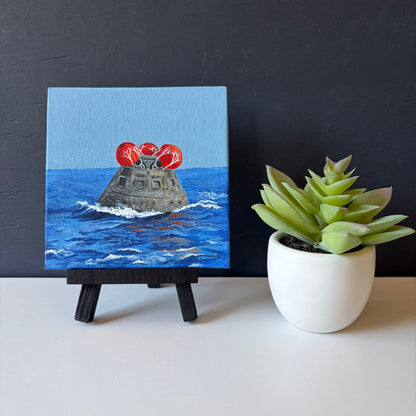 mini painting on easel of Orion capsule floating in ocean with red balloons on top