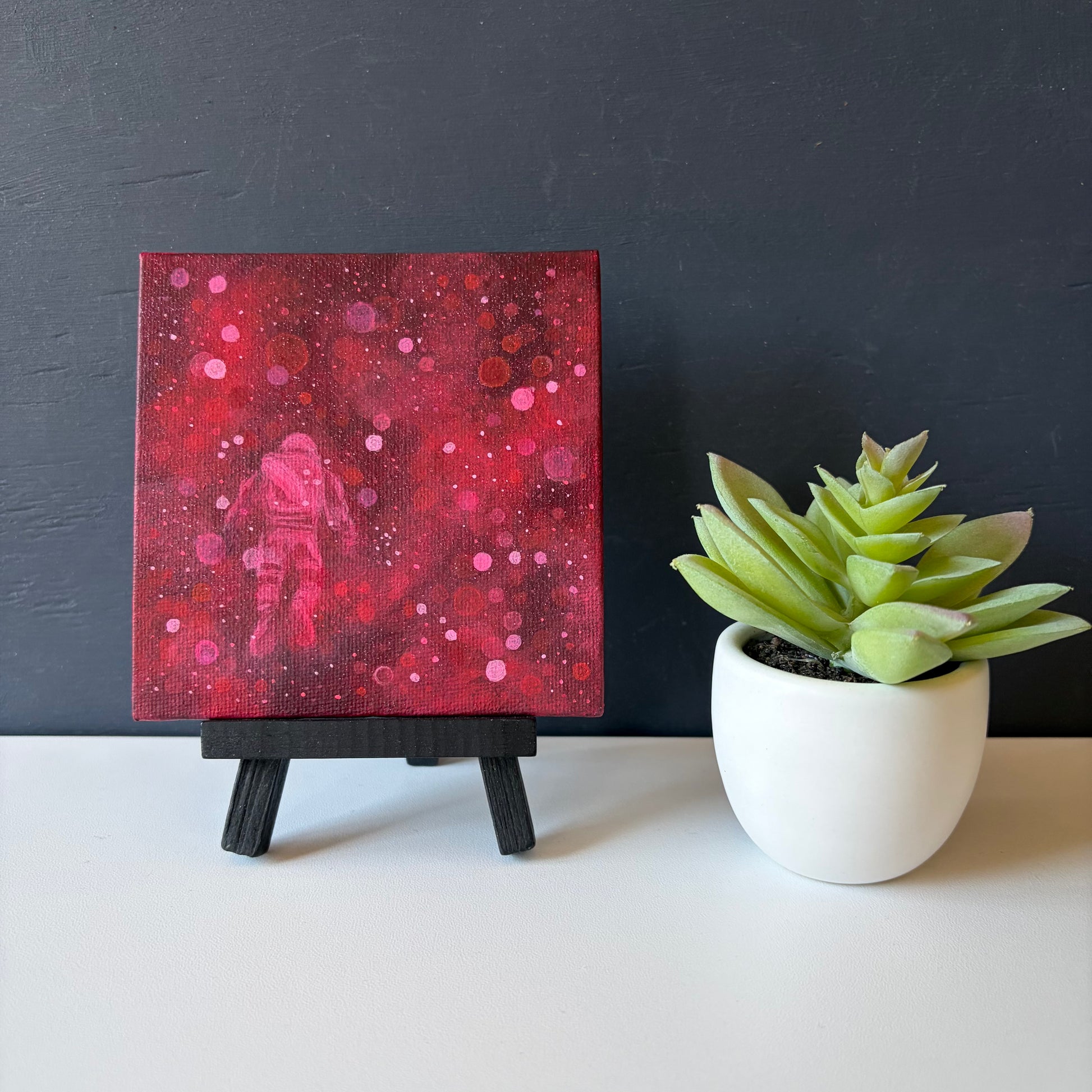 Mini painting on easel of an astronaut floating surrounded by red and pink bokeh 