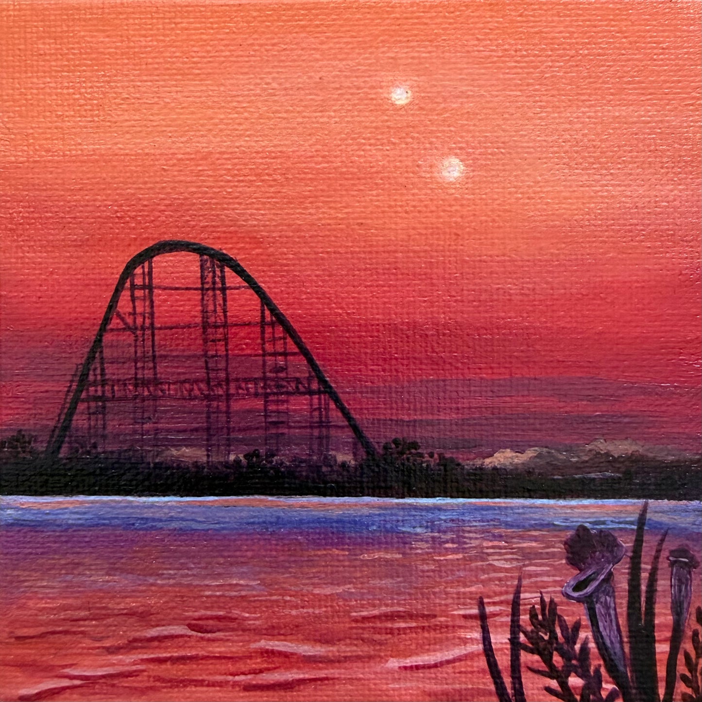 Mini painting close up. Roller coaster silhouette against a pink and orange sunset sky with water and black plants in the foreground.