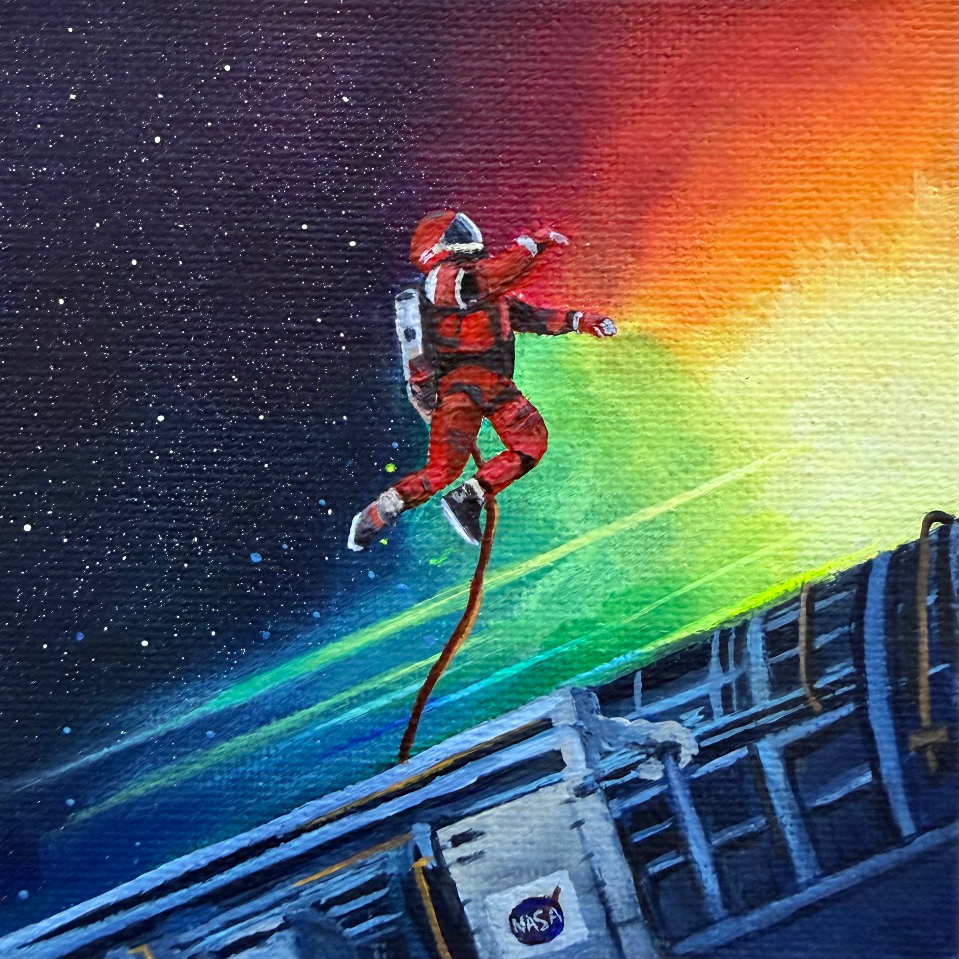 Close up of mini painting of an astronaut tethered to a spaceship with a colorful background