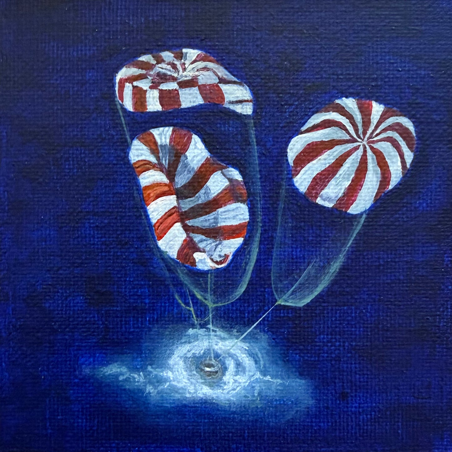 Close up of mini painting of 3 red and white striped parachutes deploying on Orion capsule landing in ocean