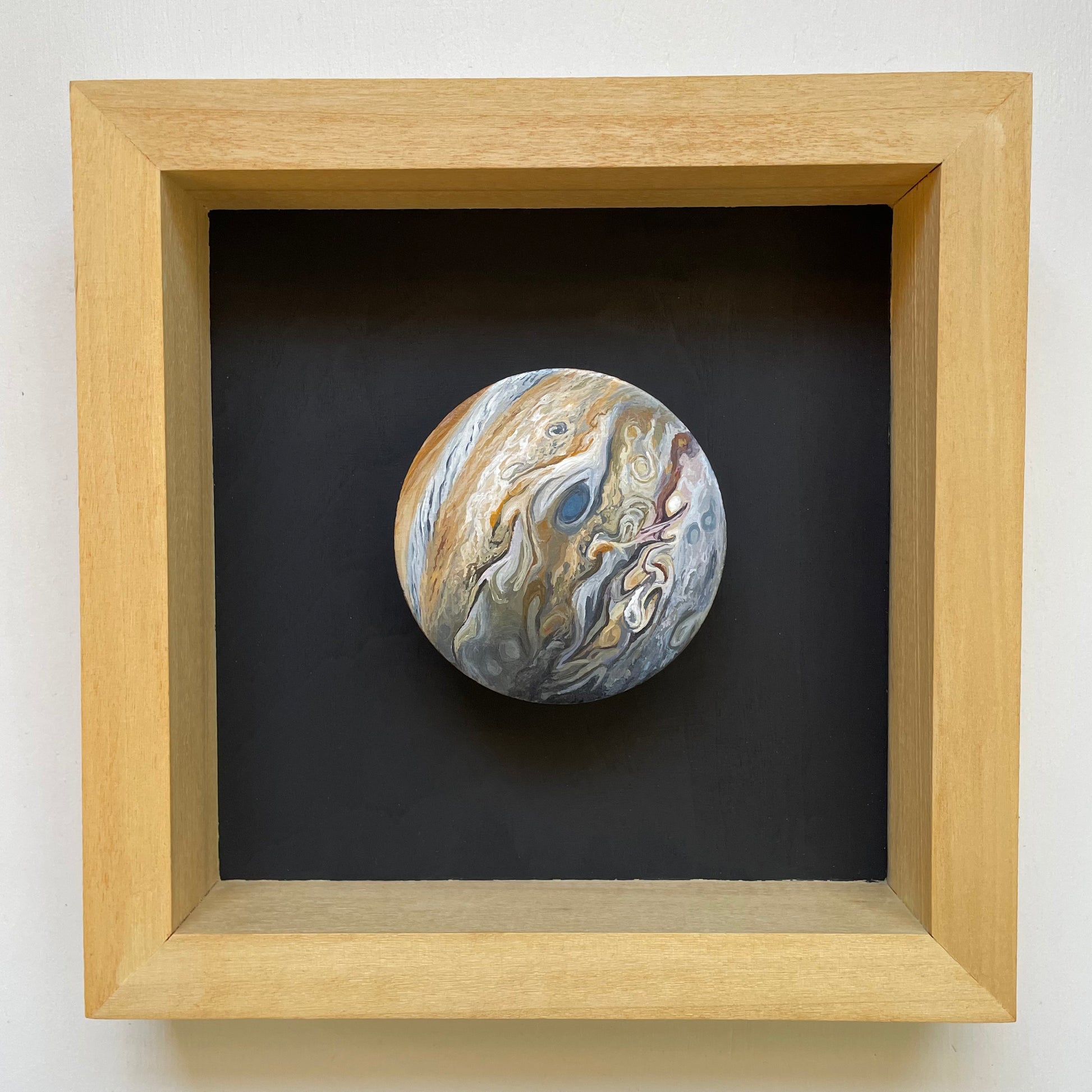 Clay disk painted like Jupiter mounted in tan stained shadowbox frame with black background