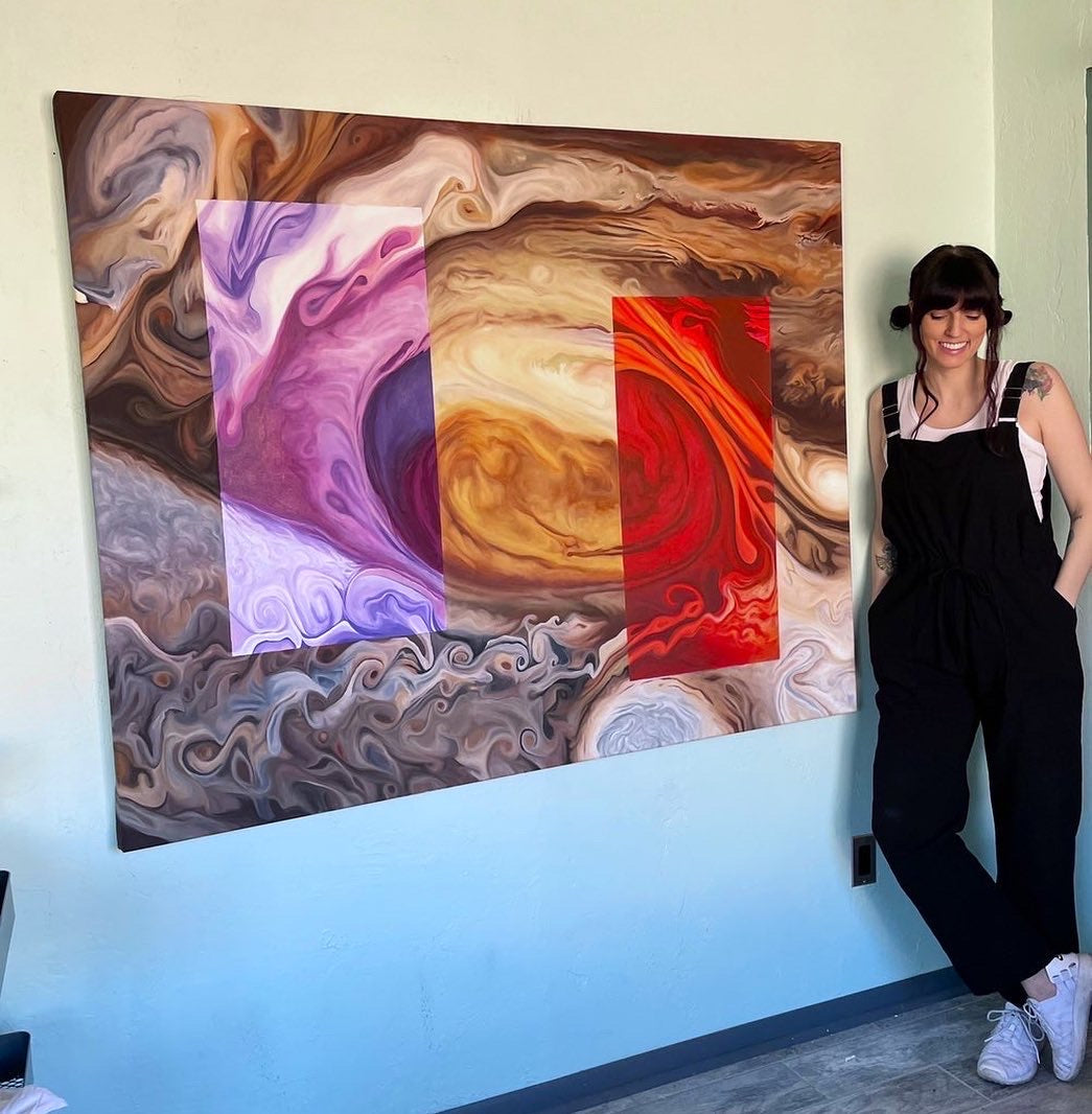 Laci standing next to a large, rectangular painting of Jupiter's Great Red Spot. There are two rectangles painted on the piece to represent how the storm looks in ultraviolet (purple) and infrared (red) wavelengths.