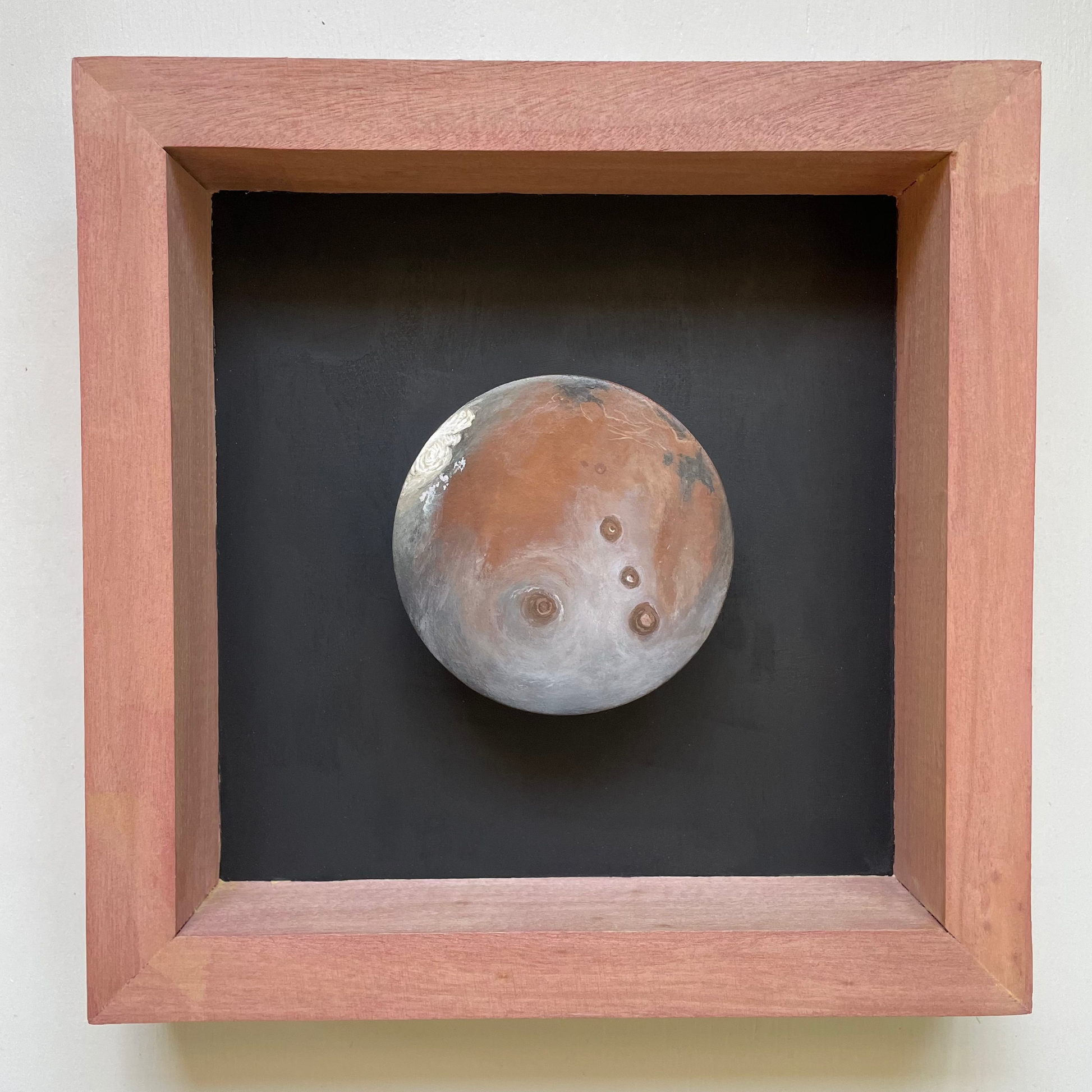 Clay disk painted like Mars in reddish stained shadowbox frame with black background