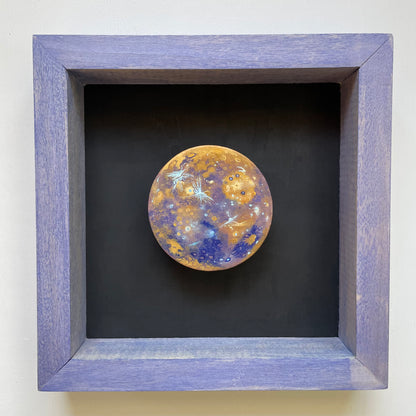 Clay disk painted like Mercury in false color mounted in blue stained wooden shadowbox frame with a black background