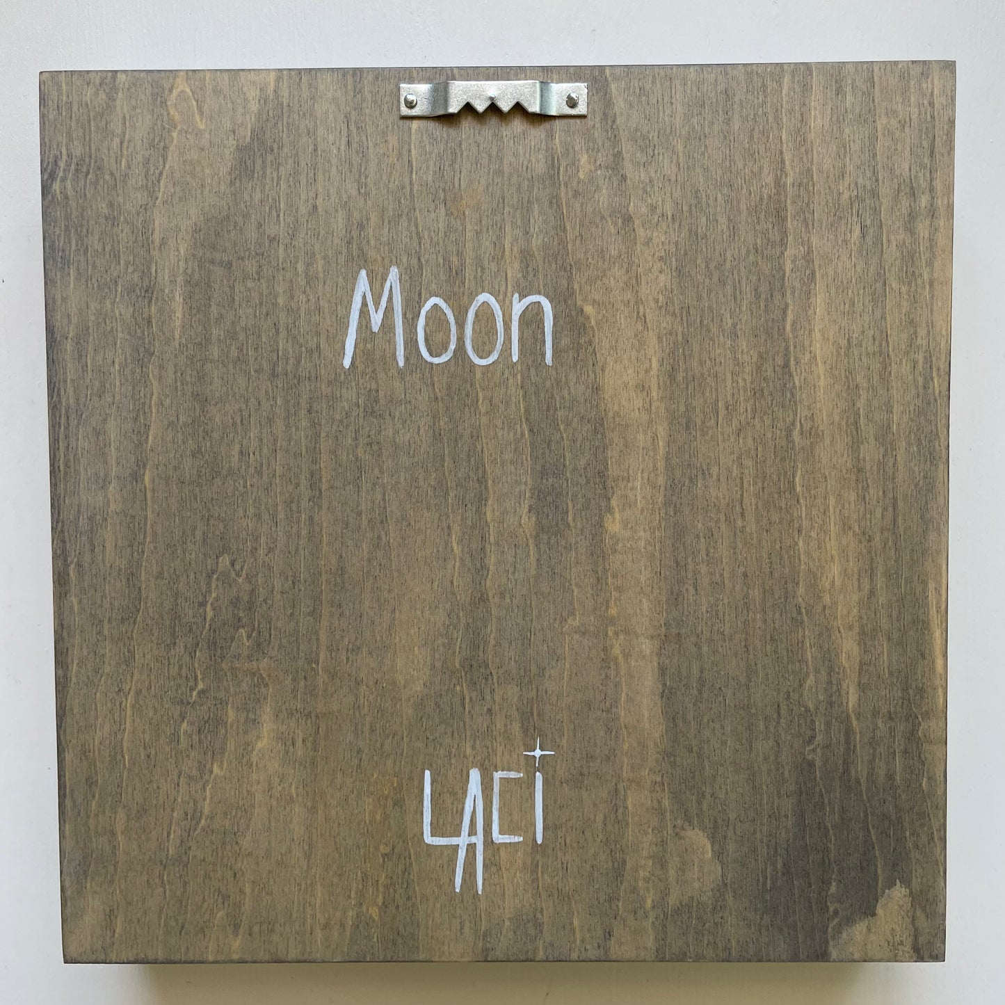 Back of shadowbox with signature, the label "Moon", and sawtooth hanger