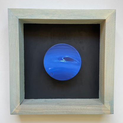 Clay disk painted like Neptune mounted in light blue shadow box with black background