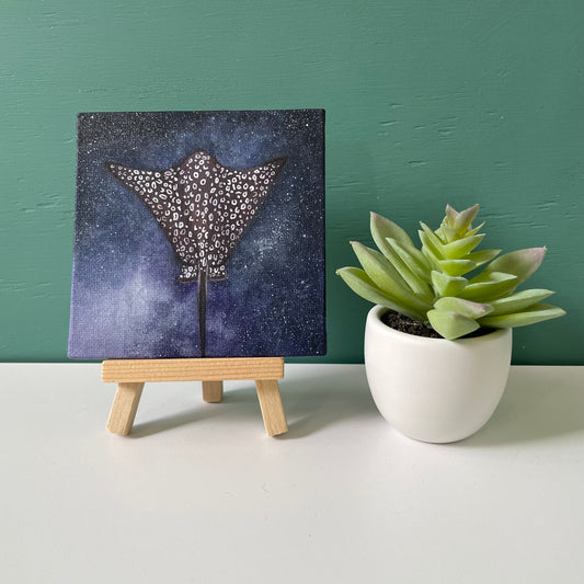 Mini painting sitting on small wooden easel next to fake succulent plant