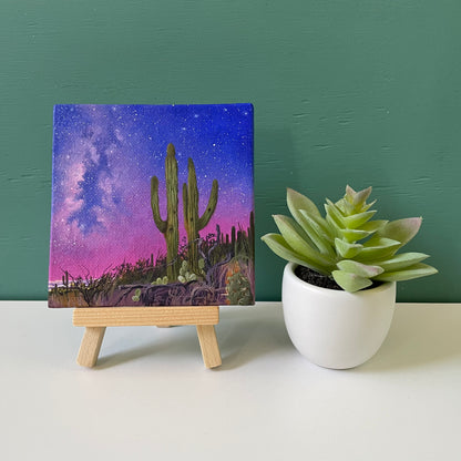 Mini painting sitting on wooden easel next to fake succulent plant