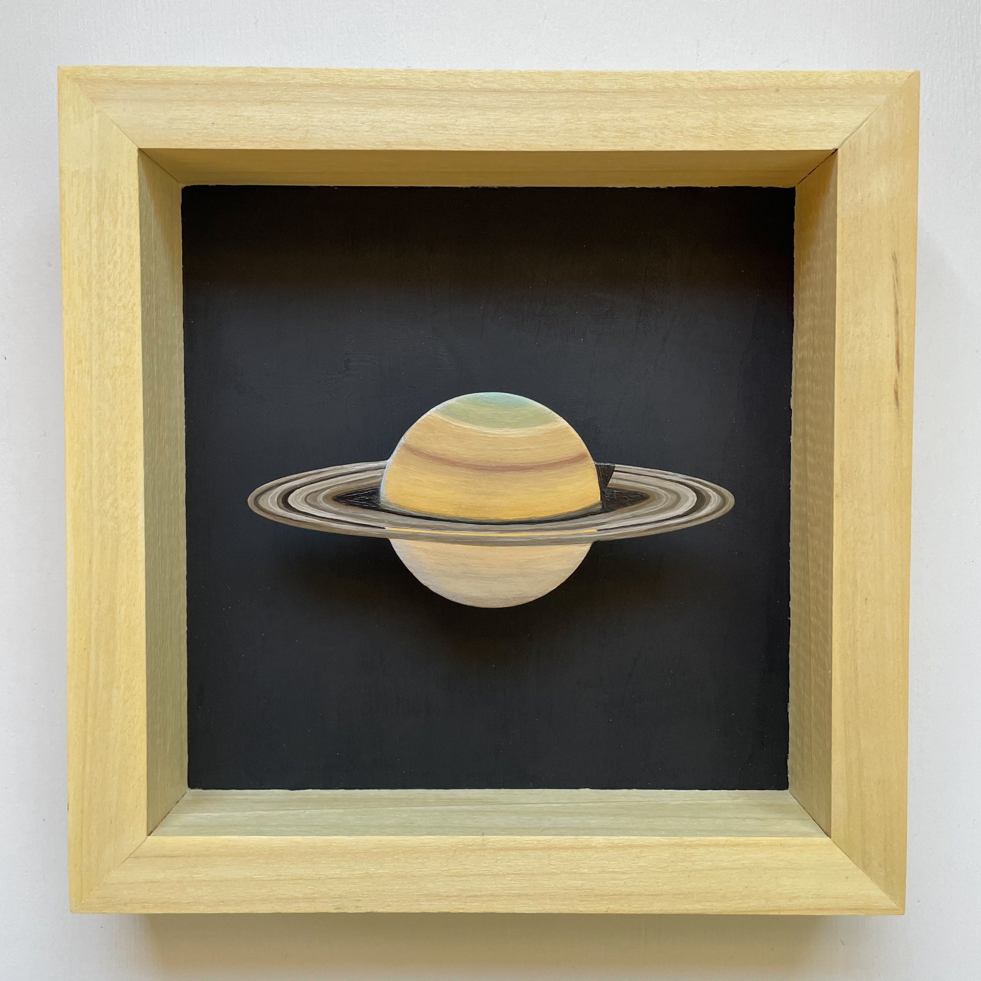 Clay Saturn mounted in yellow shadowbox frame with black background