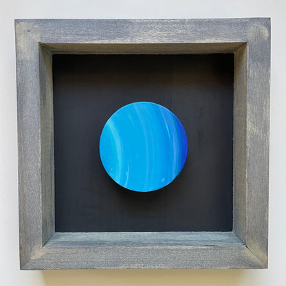 Clay disk painted like Uranus in blue grey shadowbox frame with black background